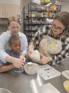 two students helping a ASL student cook